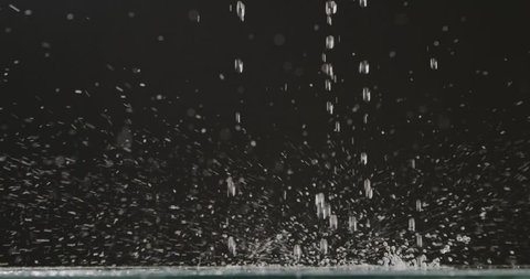 Droplets of water fall from a height on a flat surface. Water droplets and splashes scatter in different directions on a black background. Slow motion. Full HD video, 240fps,1080p