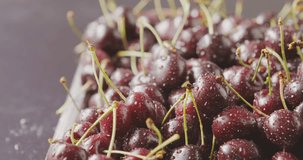 Tracking slow motion video of wet ripe red cherries on a square tray from steel. Close-up cherries background with droplets of water on berries. Soft focus. Shallow depth of field. 4K video.