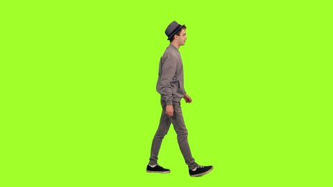 Young stylish man in hat walking on green chroma key background, Side view, 4k pre-keyed footage