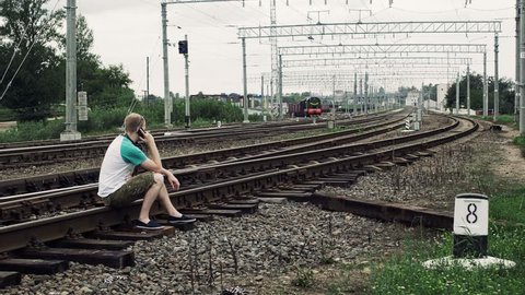 man is sitting on the railway or railroad and talkIng on the smartphone, life threatening