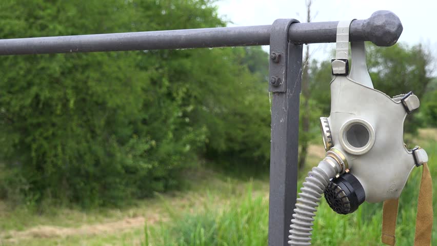 A gas mask hangs on an iron gate itnto a driveway in a rural area - closeup