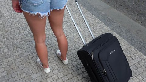 A woman with a suitcase walks down the street - closeup on the legs