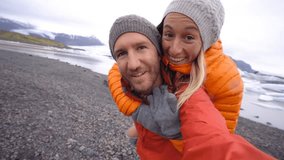 4K Video of young couple having fun taking selfie by the glacier lake at Jokulsarlon lagoon in Iceland. Two people travel love romance sharing togetherness communication concept. Springtime