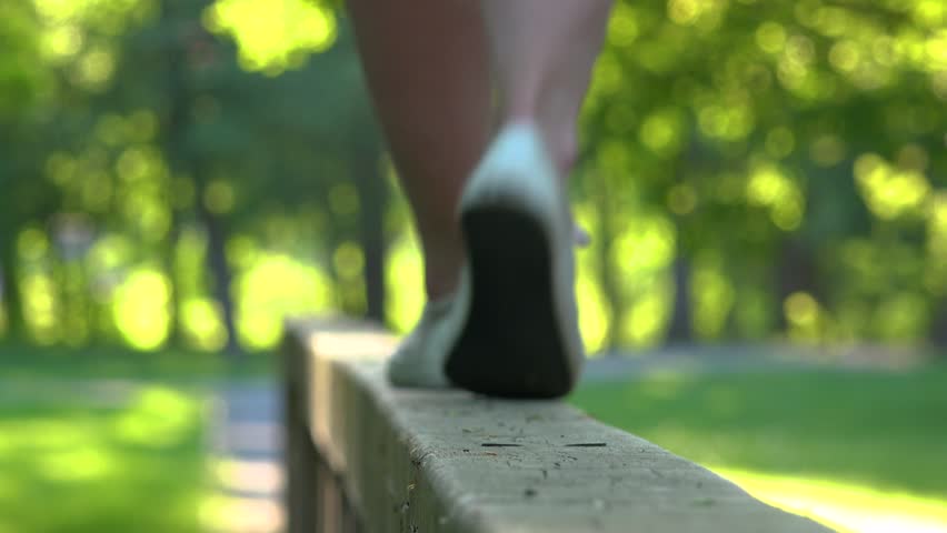 A woman in a red dress walks along a wooden railing in a park on a sunny day - closeup on the legs - unfocus