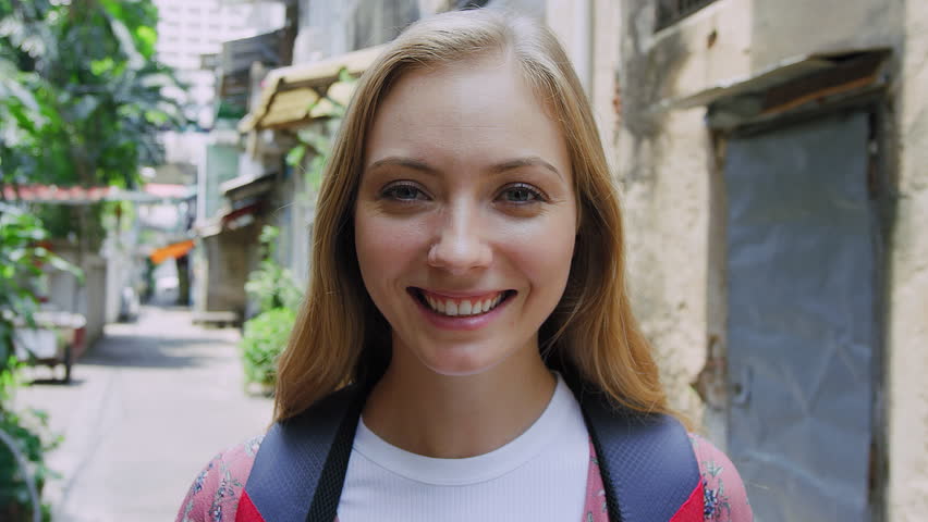Portrait of beautiful backpacker tourist girl smiling at camera on Bangkok Asian street. Slow Motion
