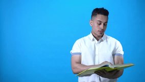 Young man wears a shirt holding a yellow book turning the pages than showing something on the left  side, on blue chroma