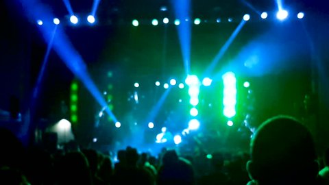 Blurred scene at a concert with laser show and people looking at the scene and dancing