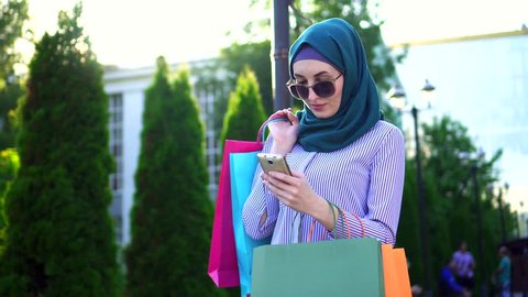 Young muslim woman in hijab bags in his hands after shopping using the phone.Sunflare