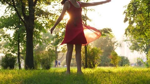 Woman dancing in red dress in summer park. Happy smiling girl enjoy life spinning around.