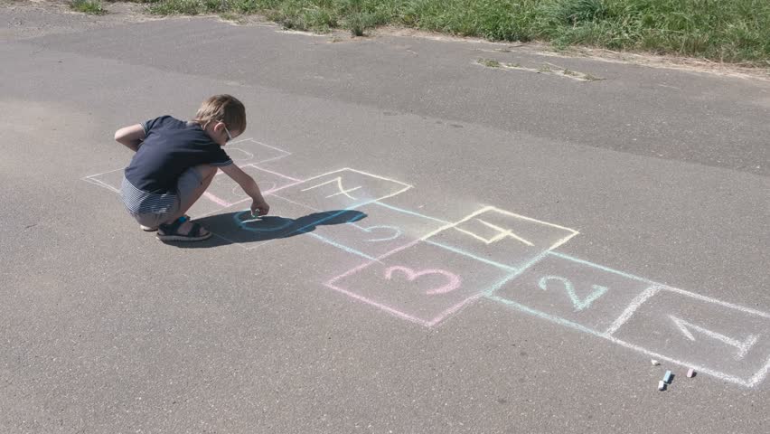 Boy is drawing hopscotch on the asphalt.