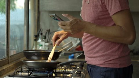 Young man using smartphone while cooking meal in kitchen 
