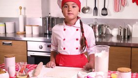 Lovely little girl in chef hat and apron baking in the kitchen at home

