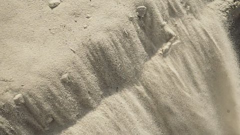White fine sand avalanche slopes down the hill under sun light. Closeup view. Slow motion