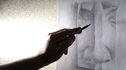 A man artist paints a plaster sketch of the nose with a graphite pencil