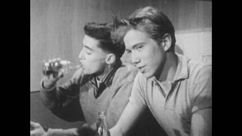 1950s: UNITED STATES: boy talks to friends. Boy watches girl at table. Boys drink soda in diner.