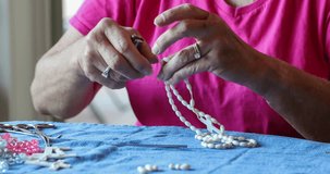 Senior woman makes a beaded rosary necklace; 4k clip