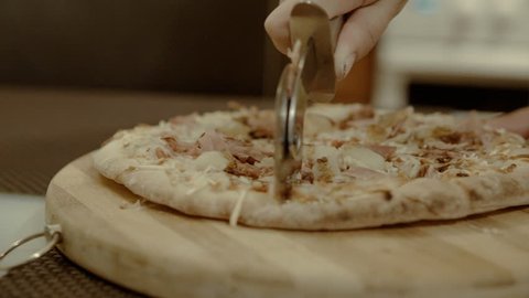 Female cuts the pizza on a wooden cutting board in the kitchen. Kitchen and homemade pizza in a close-up shot 4k. Video Stok