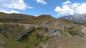 4k/60p drone footage of New Zealand grasslands showing rock formations made famous in the Lord of the Rings trilogy. Aerial video with cloud motion set against a bright blue sky.