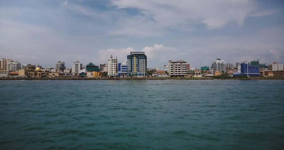 Drone flying low above the ocean water towards Colombo city coastline, Sri Lanka, modern buildings on the shore line.