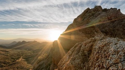 Timelapse of a partly cloudy desert sunrise viewed from a mountain pass.  Shot in HDR.  Includes hyperlapse sliding motion past rocks and in the foreground.