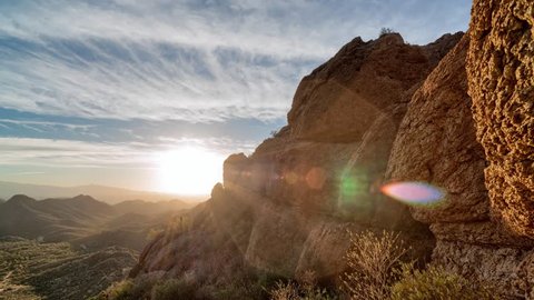Timelapse of a partly cloudy desert sunrise viewed from a mountain pass.  Shot in HDR.  Includes hyperlapse panning motion past rocks in the foreground.