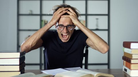 Stressed angry student screaming with open mouth while studying, reading books, cannot find any information from the textbook.