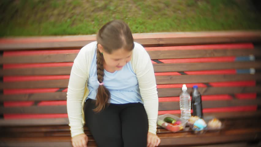 Close up of an adorable little fat girl, diving between cake and vegetables, sitting on a bench in a cafe, concept of a healthy diet 4k