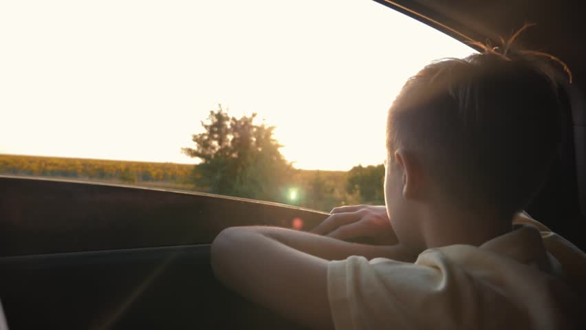 Teen boy looking out the car window Travelling in summer with family. The child looks out of the car window. Family car trip. Family vacation. A childhood dream. Boy in a car at sunset