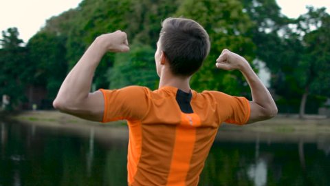 Sport athlete making biceps power pose in front of a beautiful lake in sunset