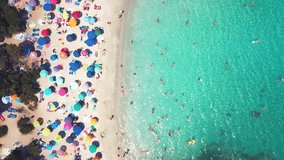 View from above, aerial view of a beautiful white beach full of colored beach umbrellas with a transparent and turquoise sea. Emerald Coast, Sardinia, Italy
