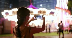 Woman taking photo and video in amusement park at night