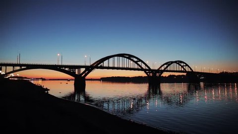 Volga bridge over Volga river after sunset, Yaroslavl region, Rybinsk city, Russia. Beautiful evening landscape with water and reflection