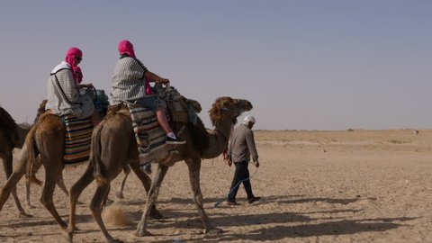 Douz, Tunisia - 10 June 2018: bedouin riding on camel on sandy desert. Tourist people astride camel traveling on Sahara desert while safari trip.