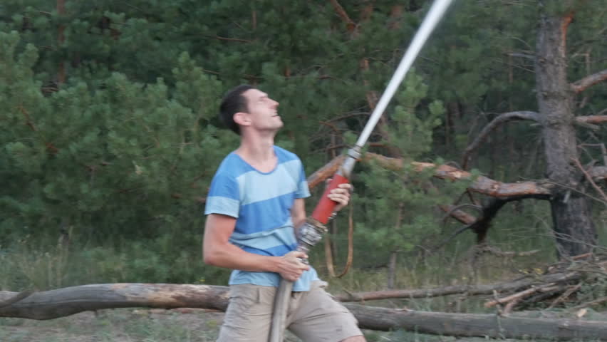 A man holds a fire hydrant in his hands with a big water jet directed upwards. A man is putting out a fire in the forest