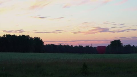 Red aerostat in the shape of a heart stands at sunset in the fields. Panoramic handheld video.