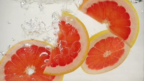 Round grapefruit slices slowly sink in water, slow motion close-up