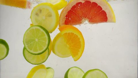 Pieces of citrus fruits lime, lemon, orange, grapefruit fall into the water with splashes and bubbles, slow motion close-up