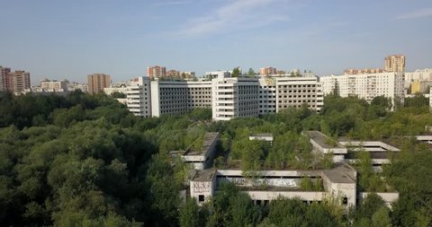 4K aerial video of dilapidated abandoned unfinished fenced off Moscow Khovrino hospital with strange triangle structure shape and Grachevka estate park area around on summer morning in Russian capital