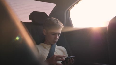 teen inside the car playing on the smartphone. Family vacation by car. The child travels by car with his family. The boy is wearing a seat belt. Vacation child with smartphone
