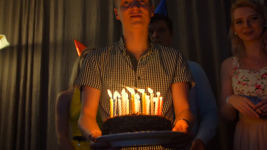 Happy male with friends bringing birthday cake to You. Camera handled movement with people, focused on candles. 4k slow motion.