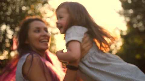 Young Mixed Race Mother and Cute Daughter Spinning Around and Hugging in Summer Park with Amazing Sunset Light Lens Flare Cinematic 4K Slowmotion.