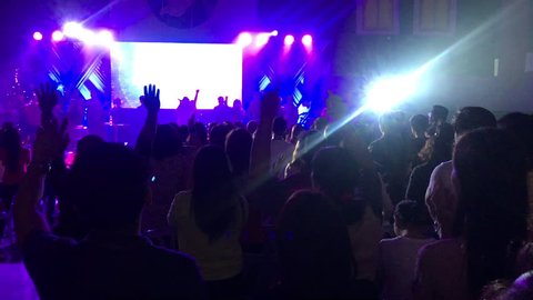 Back view of crowd from behind with hands raised up in air during a worship concert with beams of light