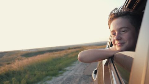 Teen boy looking out car window. Summer trip with family. Boy is dream. Happy boy traveling with family. Dream kid. Happy family traveling by car. Smile of kid in car window