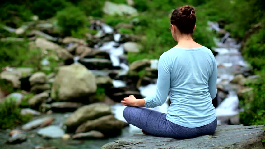 Young sporty fit woman doing yoga - meditating in Padmasana (Lotus Pose) outdoors at tropical waterfall. Himachal Pradesh, India