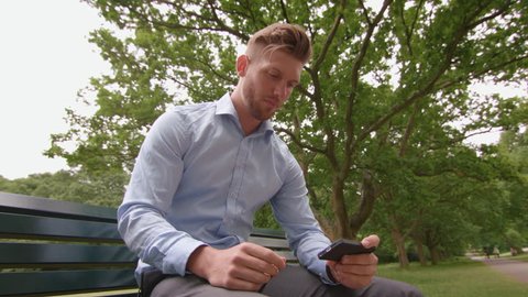 Man Sat on Bench in Park Watching Sports Match on His Phone In Slow Motion