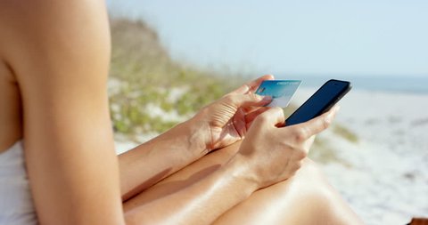 Woman using credit card on vacation shopping online with mobile phone at the beach close up RED DRAGON