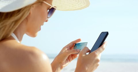 Woman using credit card on vacation shopping online with mobile phone at the beach RED DRAGON