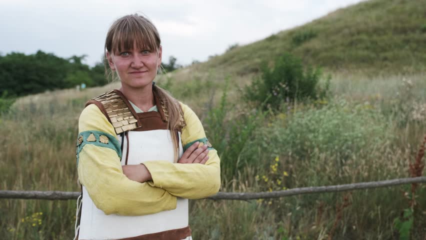 A view of a young woman, wearing ethnic costume, standing in a field with crossed hands