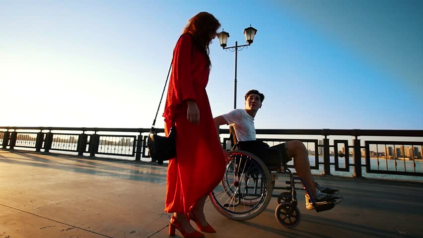 Young Disabled Man On A Walk With A Beautiful Girl On The Waterfront In The Summer Evening