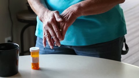 HD clip of a senior woman with arthritic pain, rubbing hands together near a prescription bottle of painkillers on the table near her